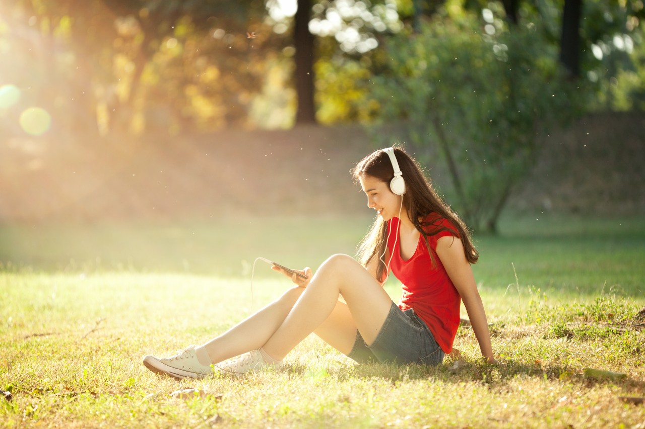 Jakého vybrat mobilního operátora - dívka s mobilním telefonem a sluchátky na louce